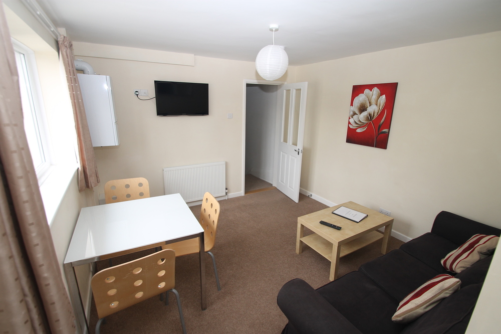 Living area with black two-seater sofa, wall mounted tv, white dining table with three chairs and coffee table