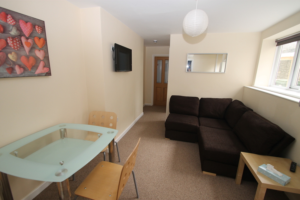 Living space with L shaped sofa, glass dining table with two chairs, wall mounted tv and coffee table