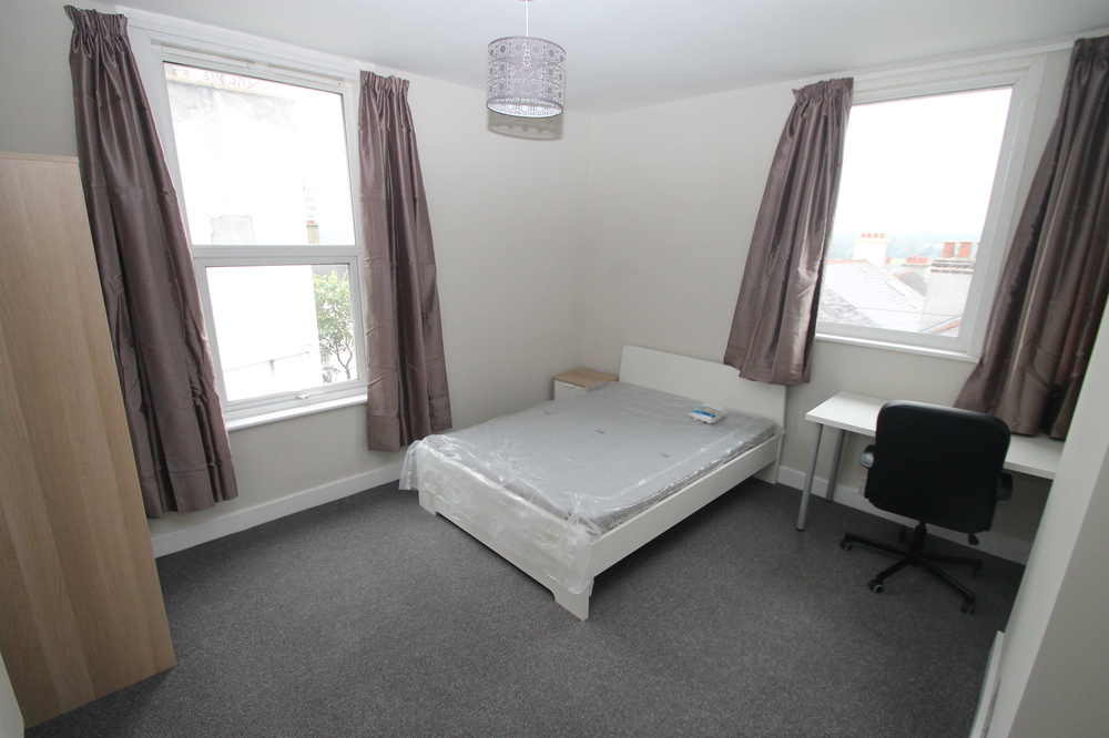 student bedroom with double bed, bedside table, white desk with black office chair and two door wardrobe