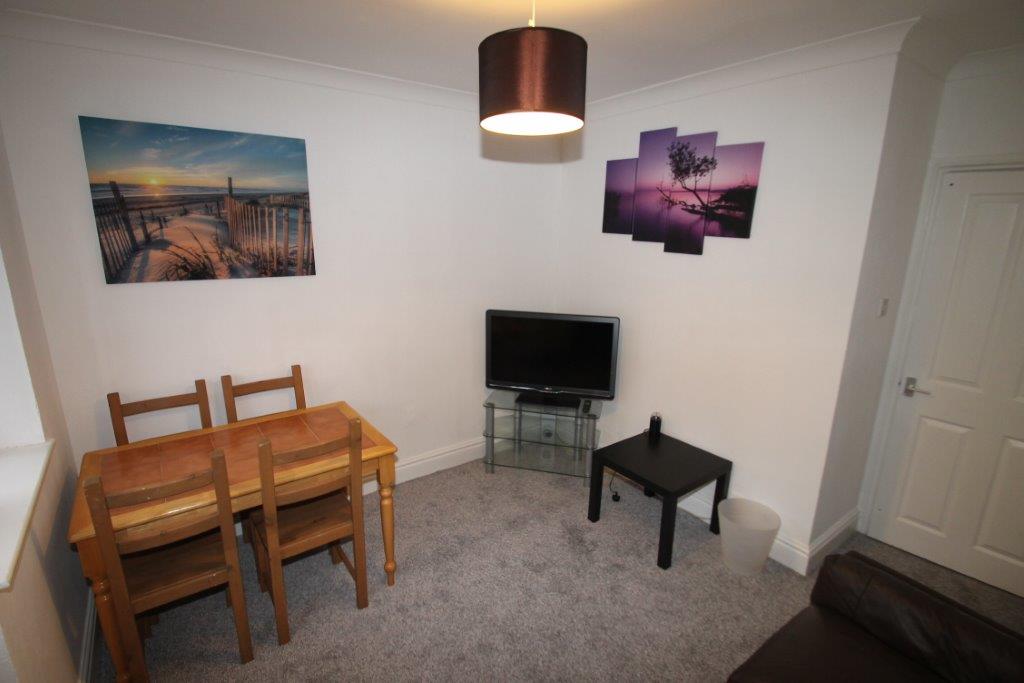 living area with dining table with four dining chairs, tv on tv stand and black lather sofa