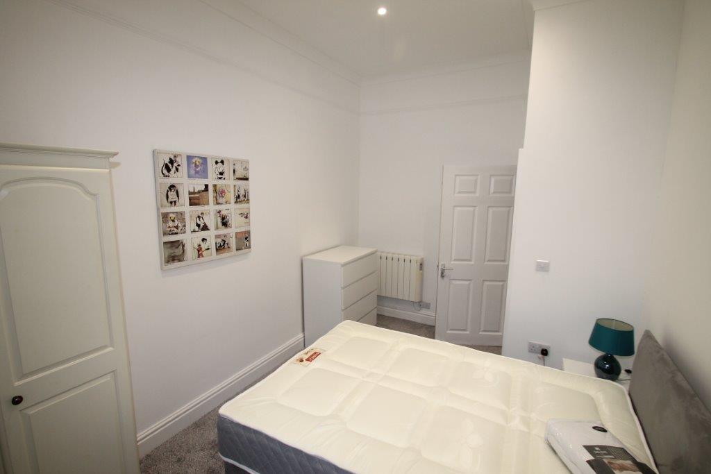 student bedroom with double bed, chest of drawers, bedside table with lamp and white two door wardrobe