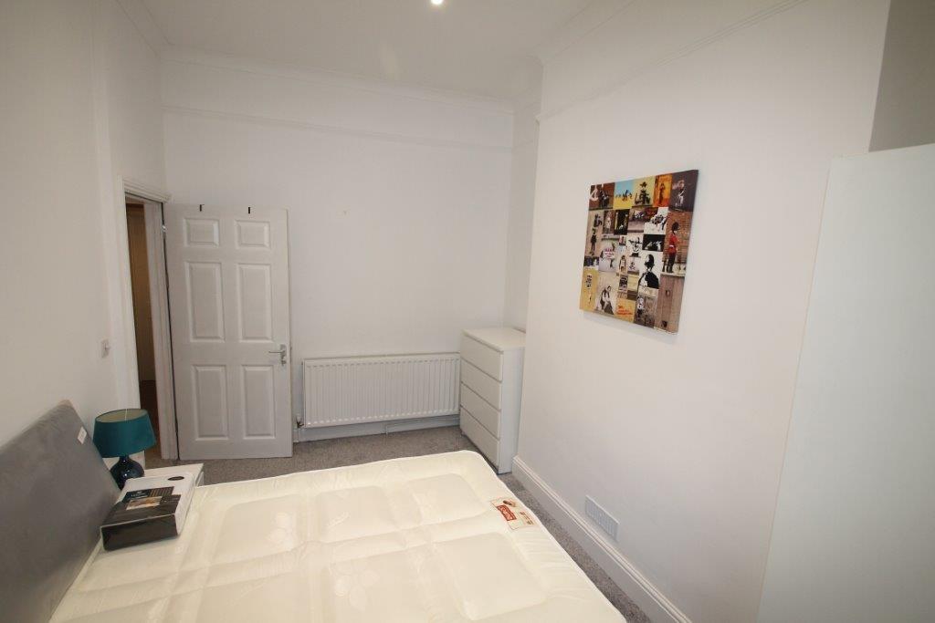 student bedroom with double bed, white chest of drawers, white bedside table and banksy canvas mounted on wall