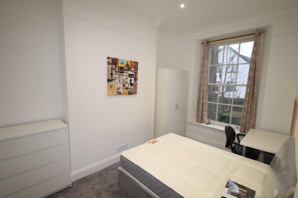 student bedroom with double bed, chest of drawers, two door white wardrobe, desk with black office chair and pinboard above desk