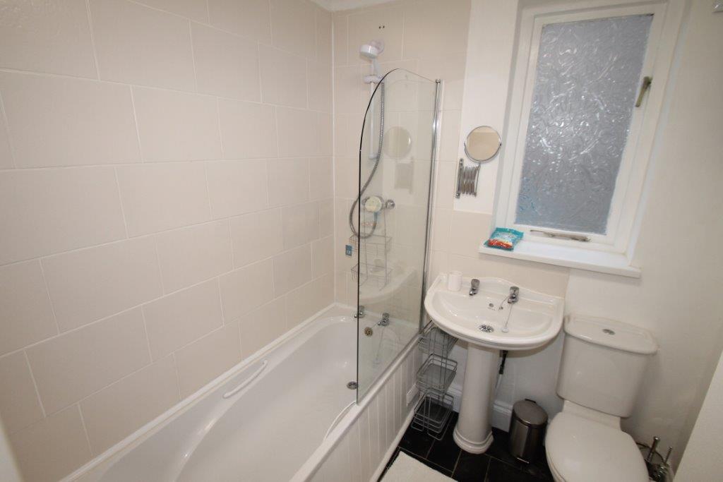 shared bathroom with bath with shower head and circular mirror by sink