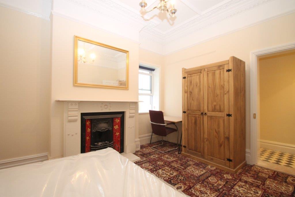 Student bedroom with double bed, two door wardrobe, white feature fireplace and desk