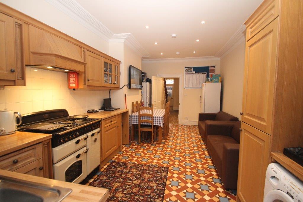 Shared kitchen with fridge freezer, large cooker with hobs, washing machine leading to living area with two double seater sofas with tv mounted on the wall