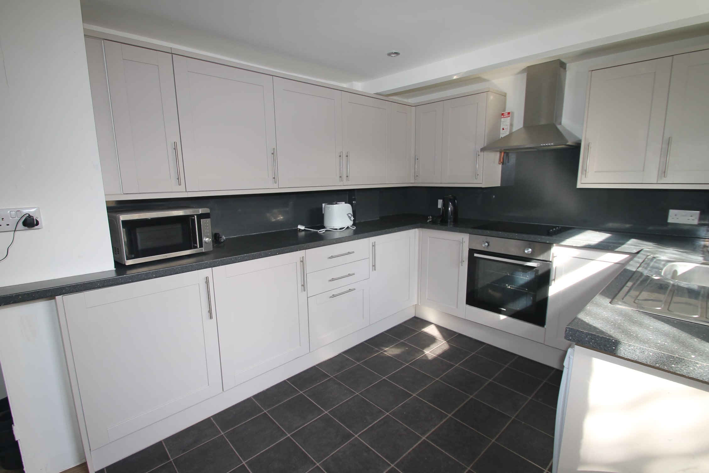 White shared kitchen with induction hobs and cooker, microwave and sink