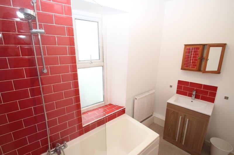 red tiled bathroom with shower head and mirrored cupboard above sink