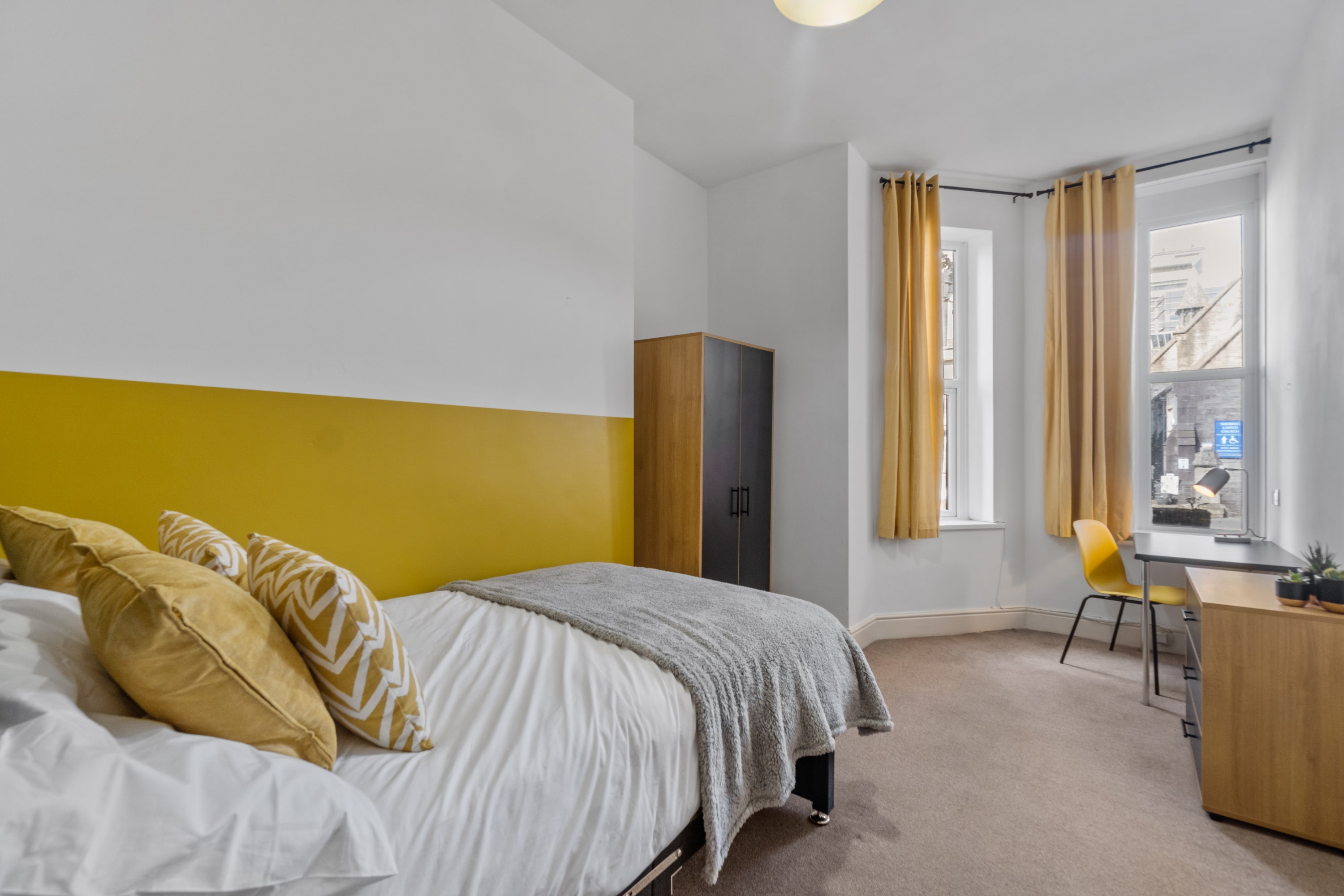 student bedroom with double bed, two door wardrobe, chest of drawers, desk with yellow chair
