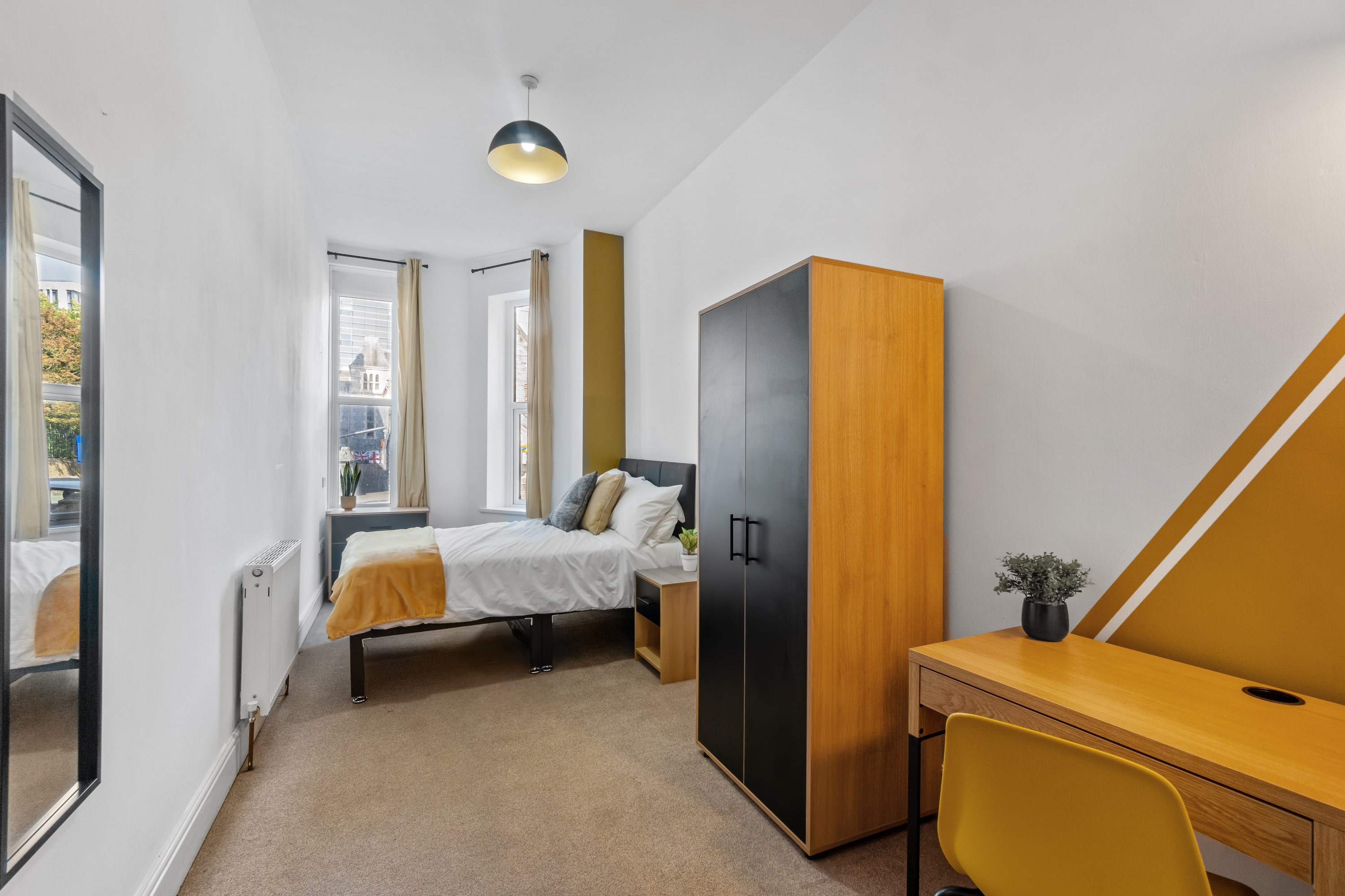 student bedroom with double bed, bedside table, two door wardrobe, yellow desk with yellow chair, full length mirror