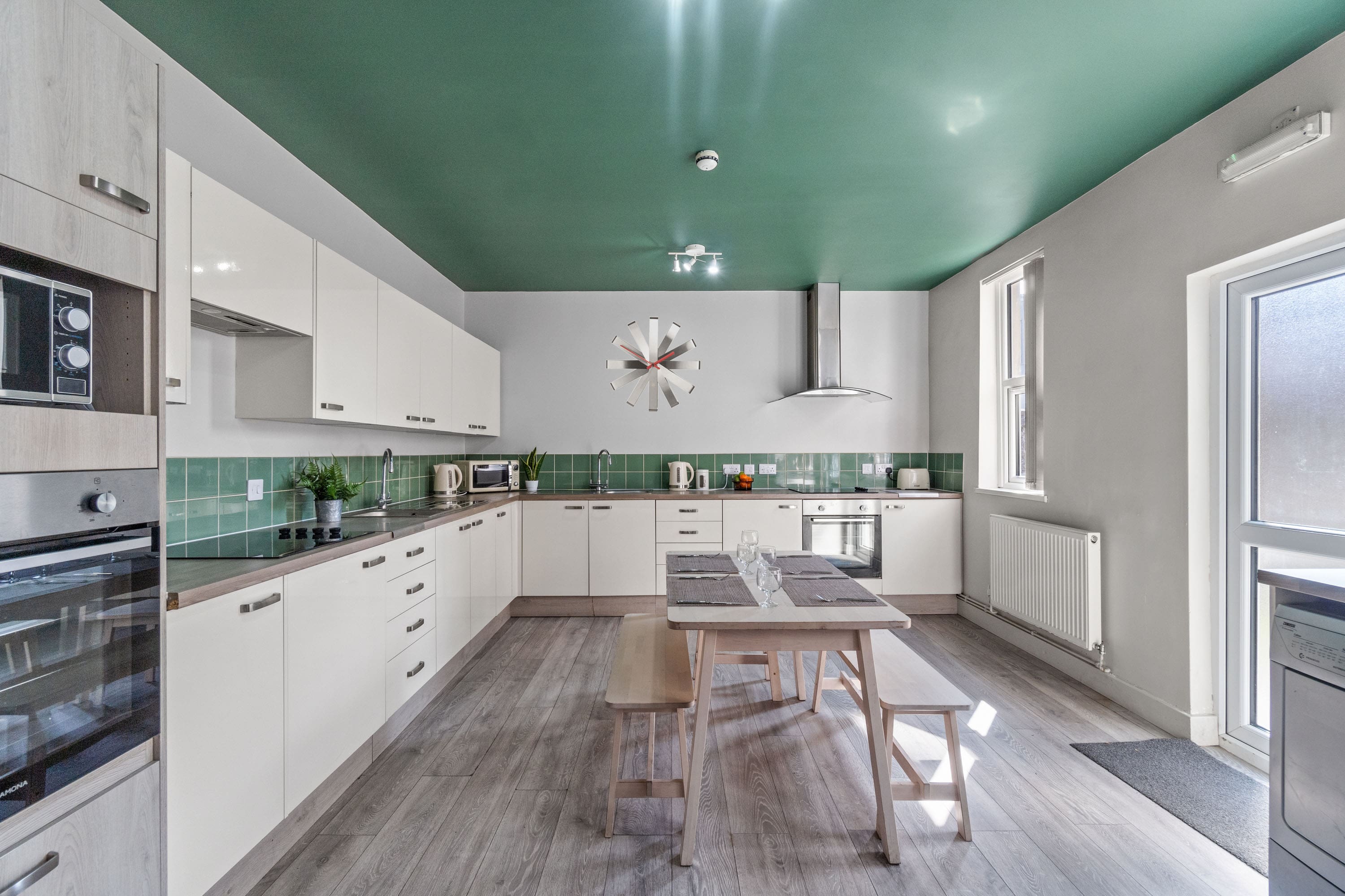 white modern kitchen with two cookers with induction hobs, dining table in the middle of room with bench seating