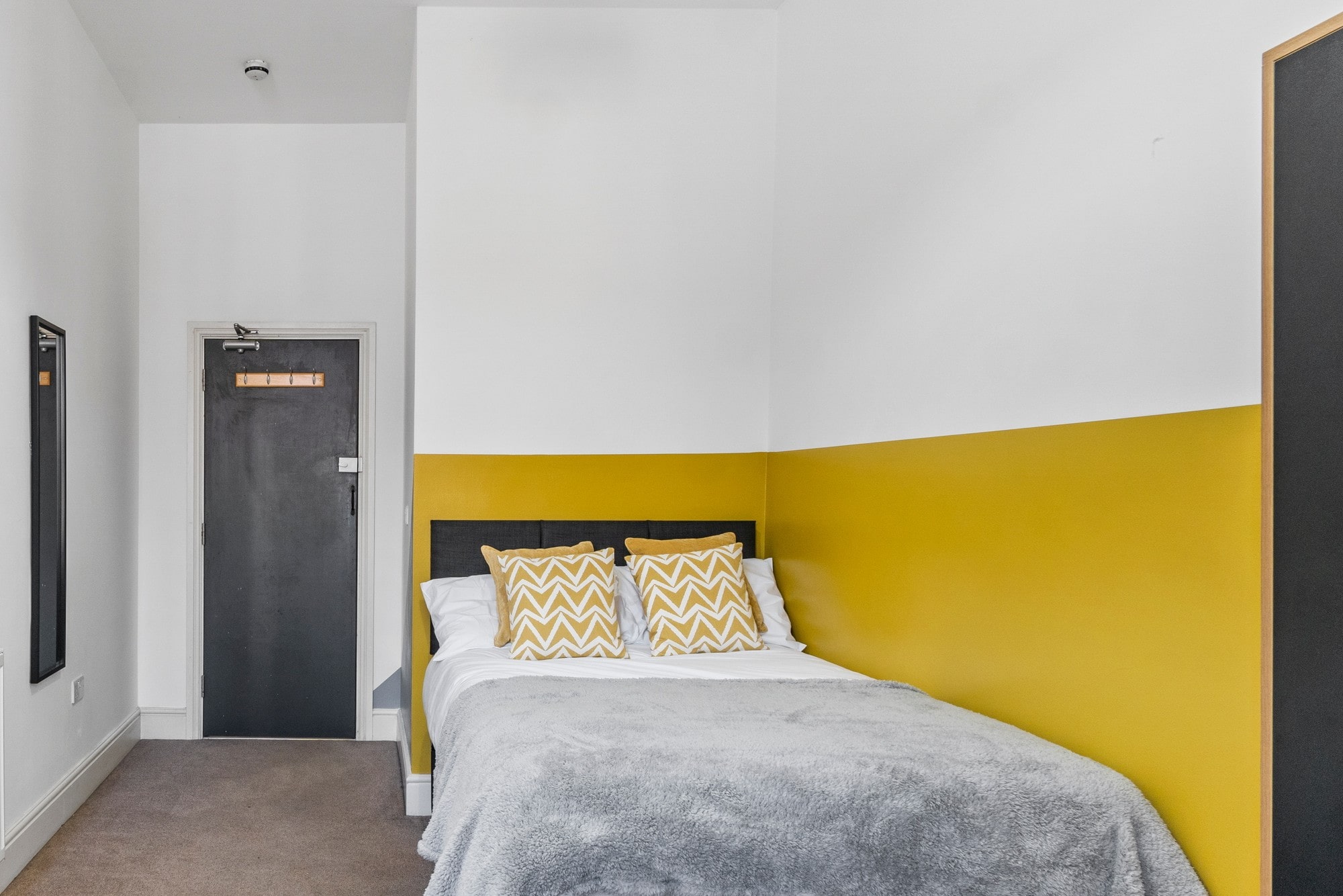 student bedroom with double bed, yellow feature wall and black full length mirror