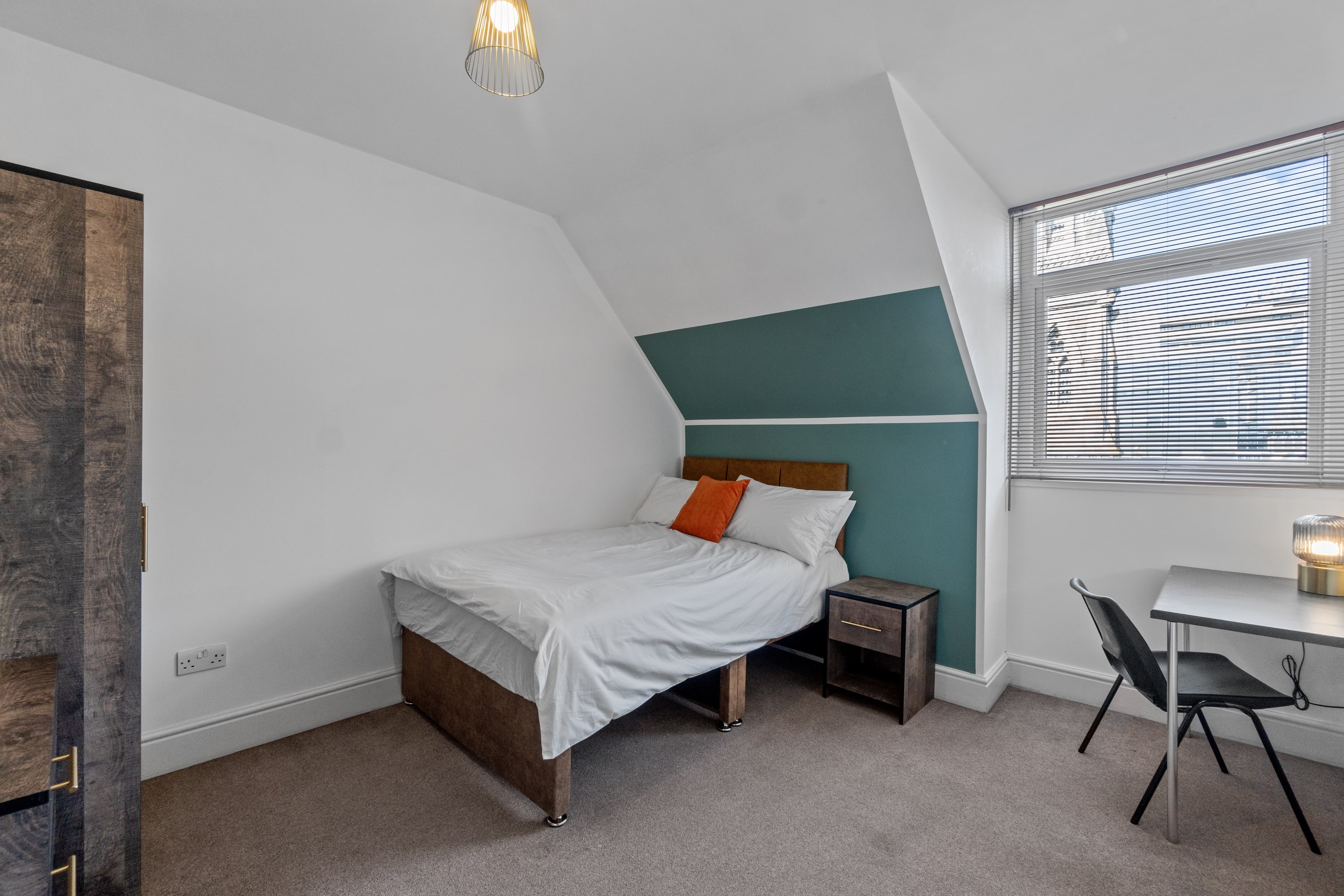student bedroom with double bed, two door wardrobe, bedside table, desk with black chair