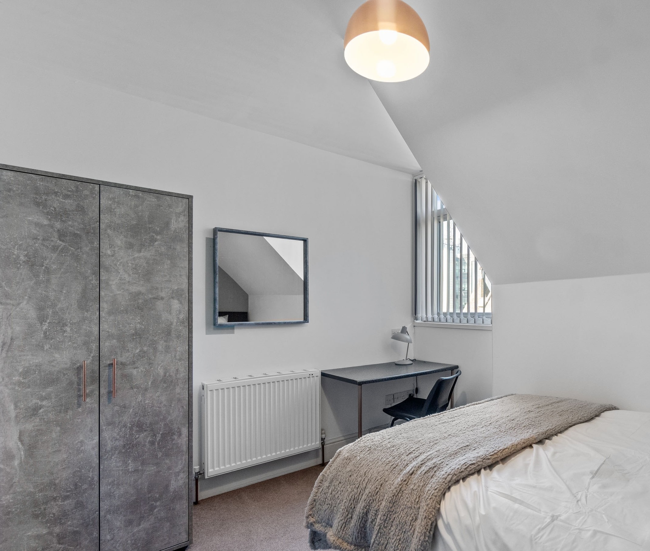 student bedroom with double bed, two door wardrobe, desk with black chair and wall mounted mirror