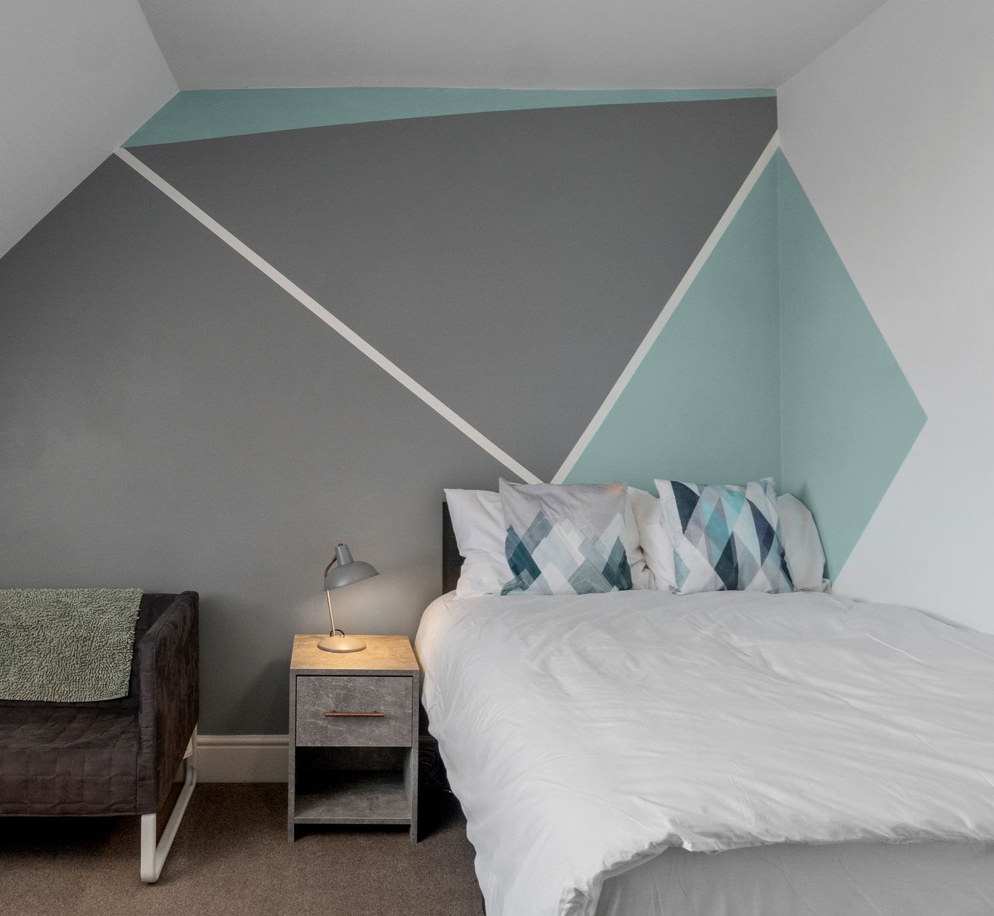 student bedroom with double bed, bedside table with grey lamp and black sofa