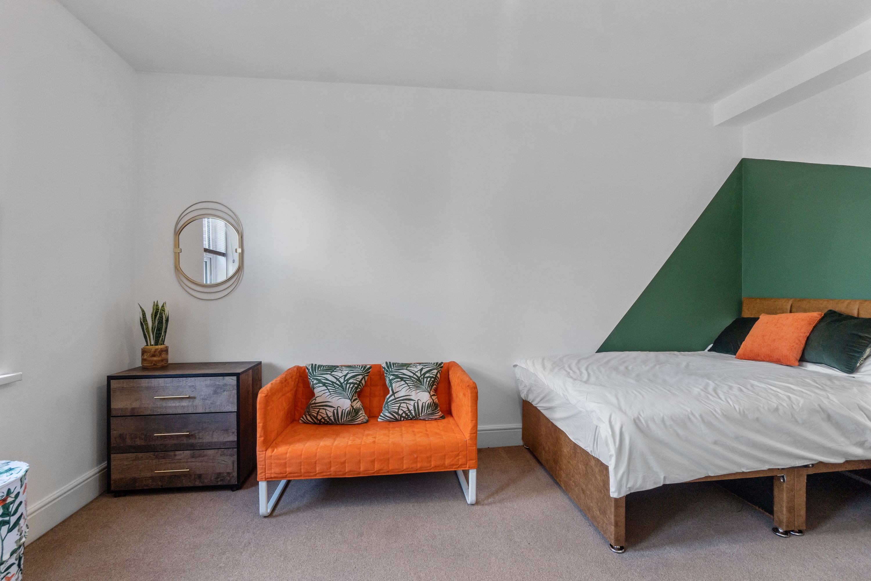 Student bedroom with double bed, chest of drawers, small orange sofa and small green feature wall
