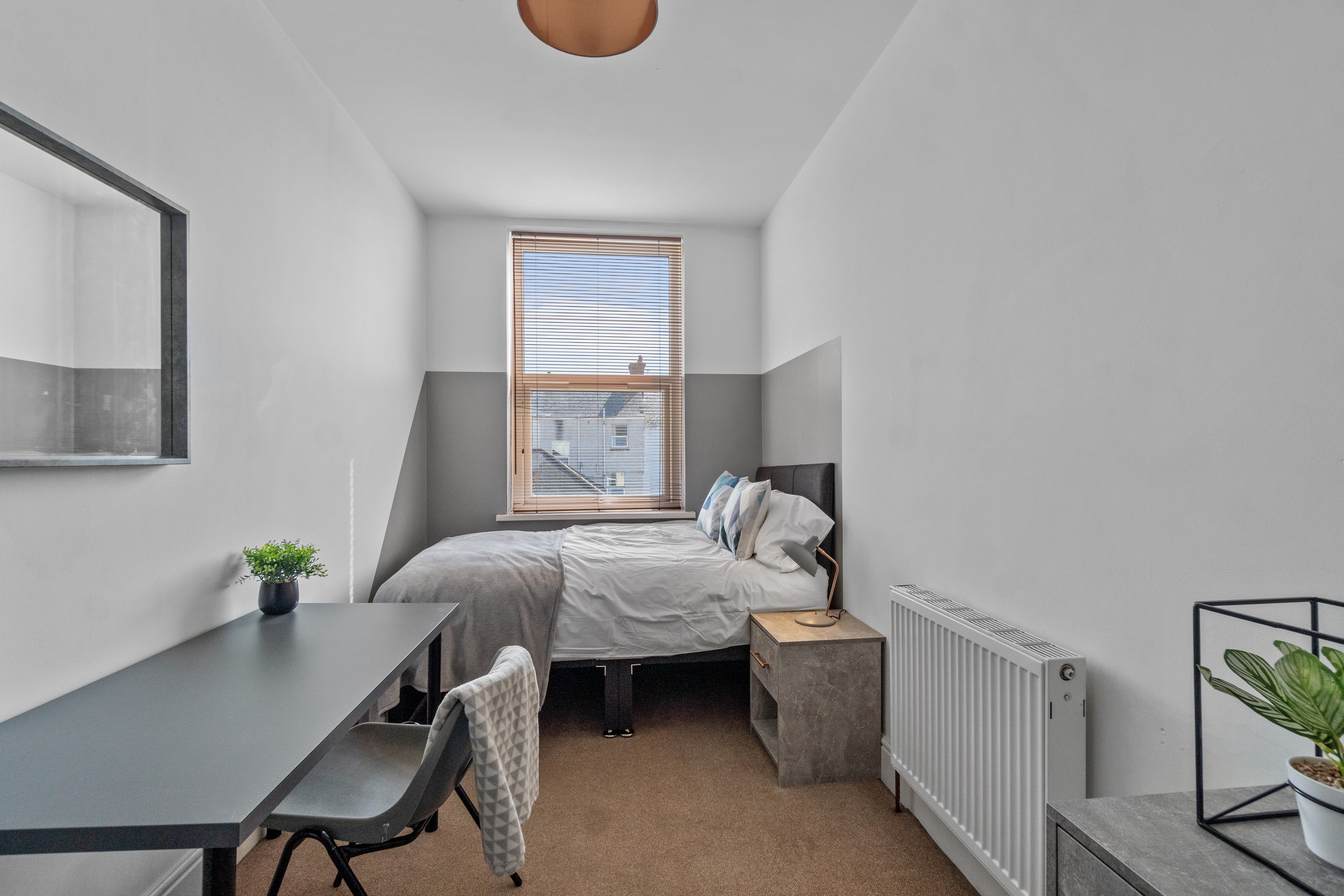 student bedroom with double bed, bedside table, desk with grey chair, chest of drawers and wall mounted mirror