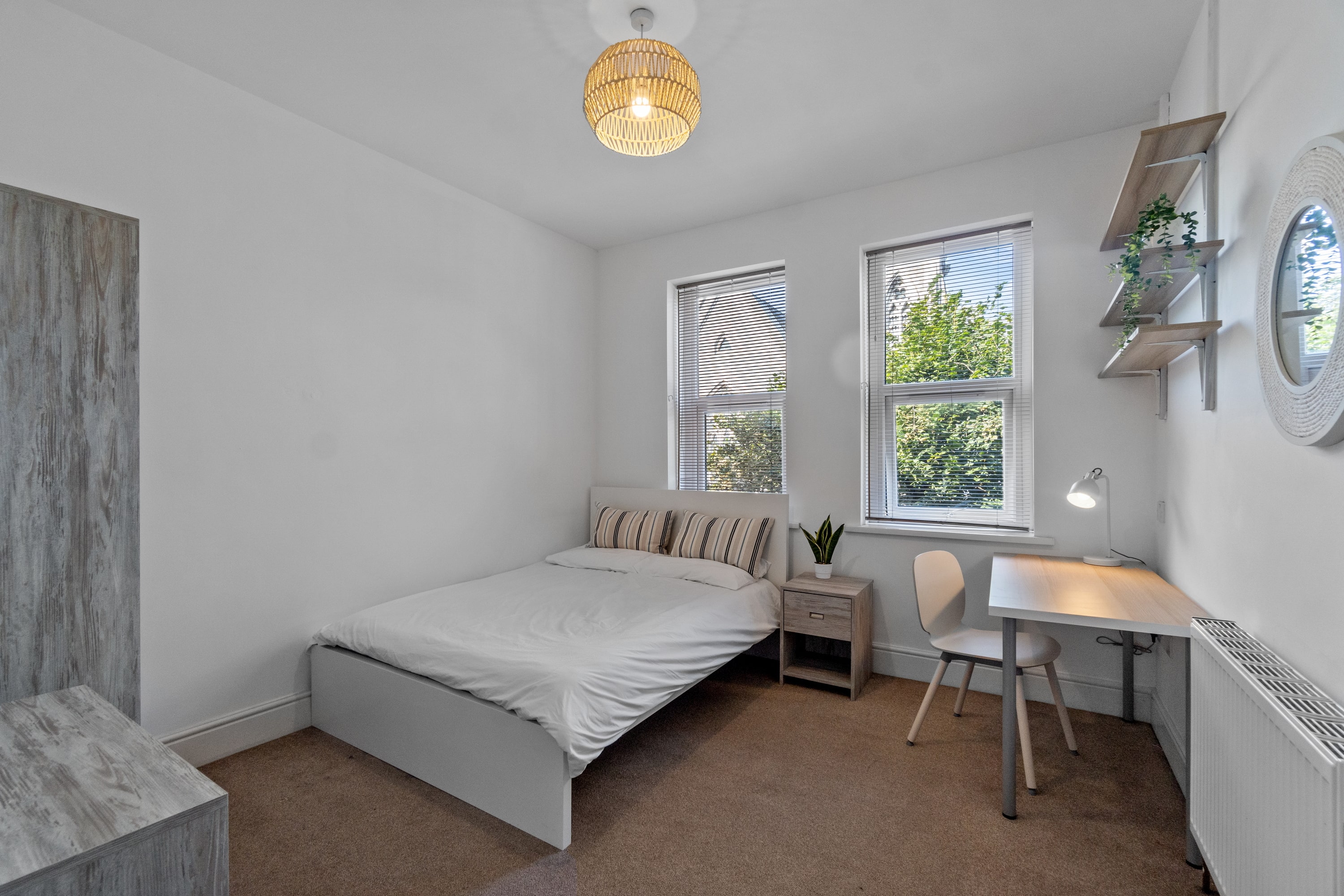 student bedroom with double bed, grey two door wardrobe, chest of drawers, desk with chair and bedside table