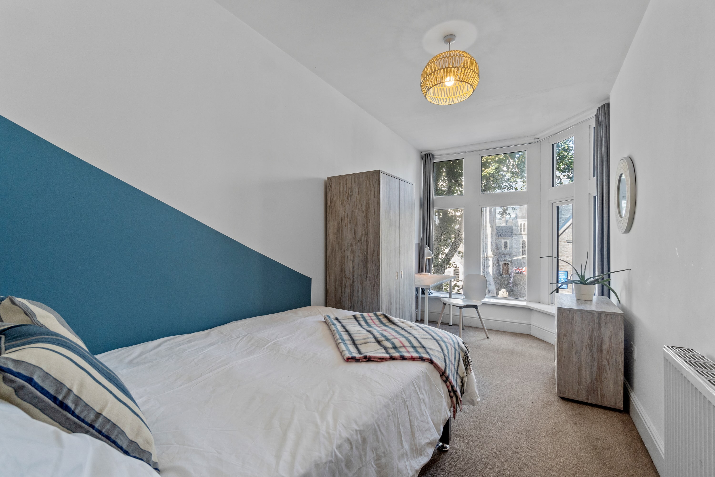 student bedroom with double bed, grey two door wardrobe, desk with white chair and chest of drawers