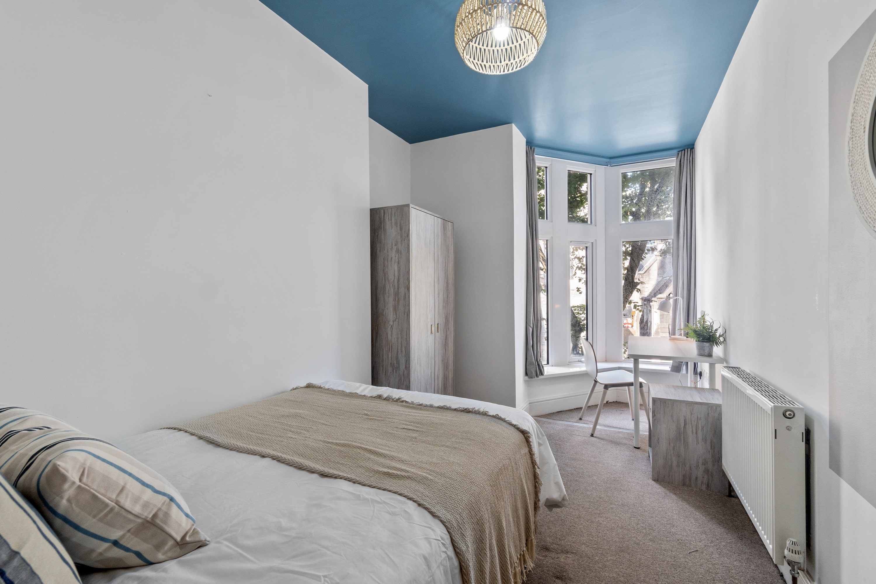 Student room with double bed, two door wardrobe, desk with white chair and grey bedside table