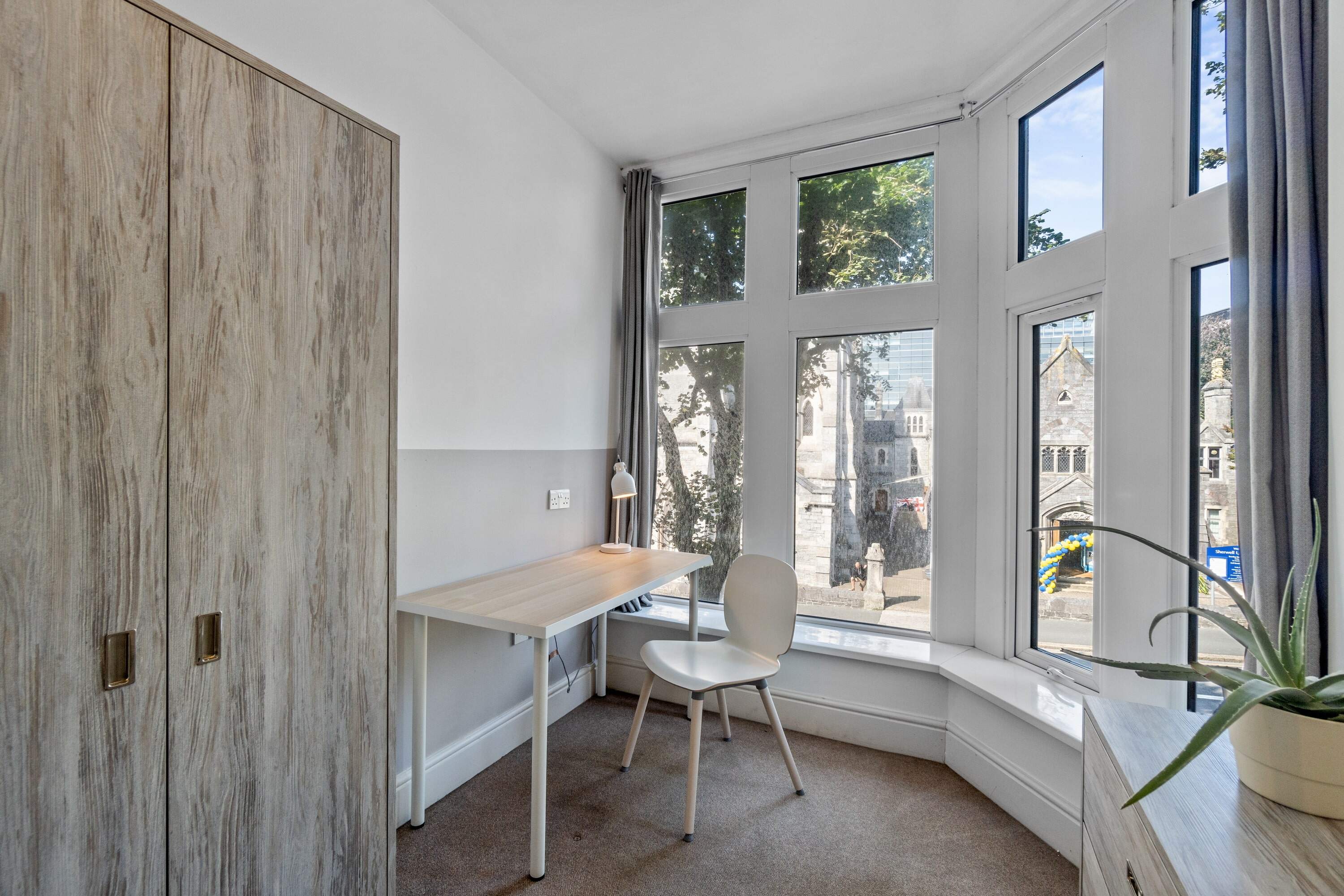 student room with desk, two door wardrobe, desk with white chair, chest of drawers and large windows