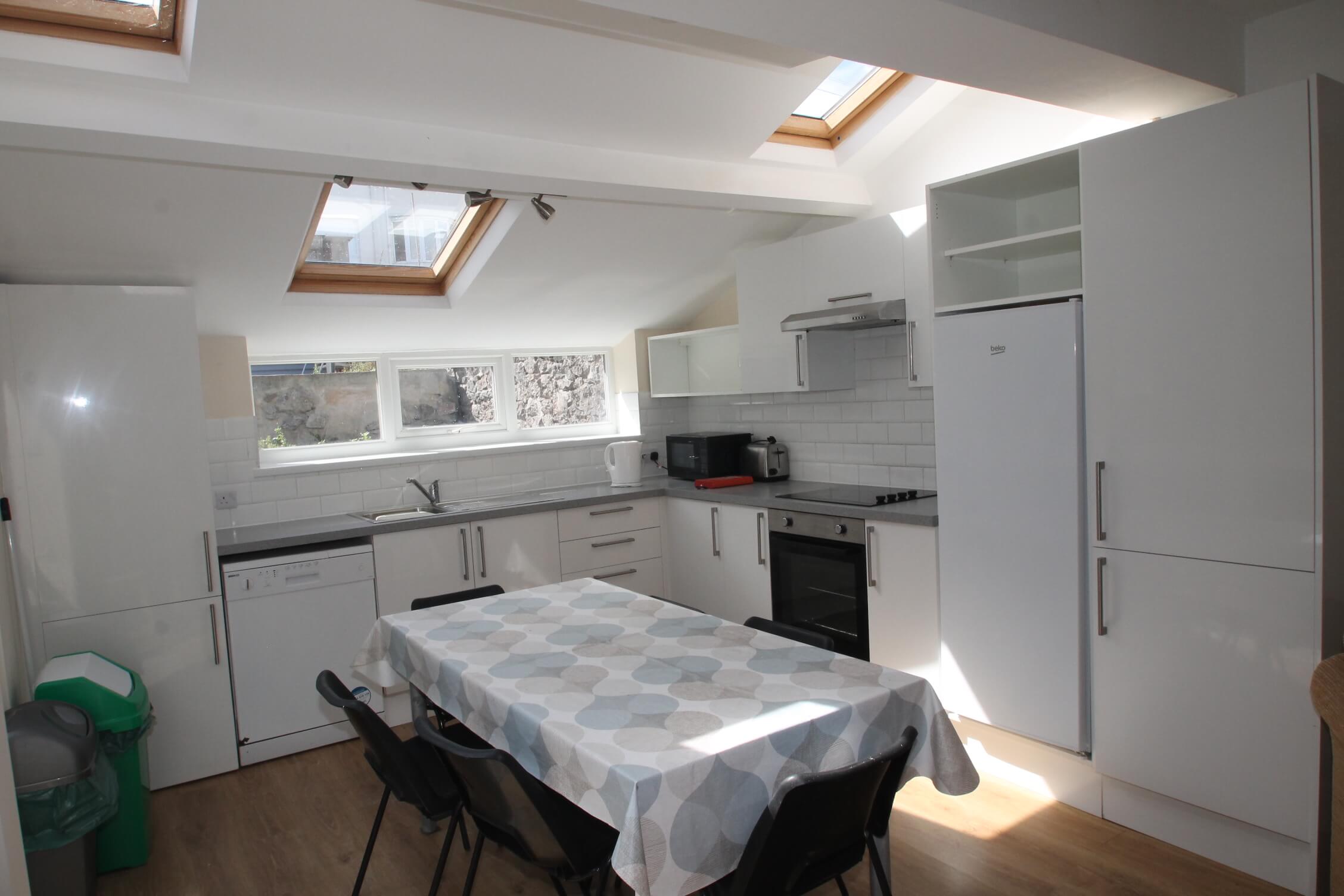 white kitchen with induction hobs and cooker, dishwasher, fridge freezer and dining table with six chairs