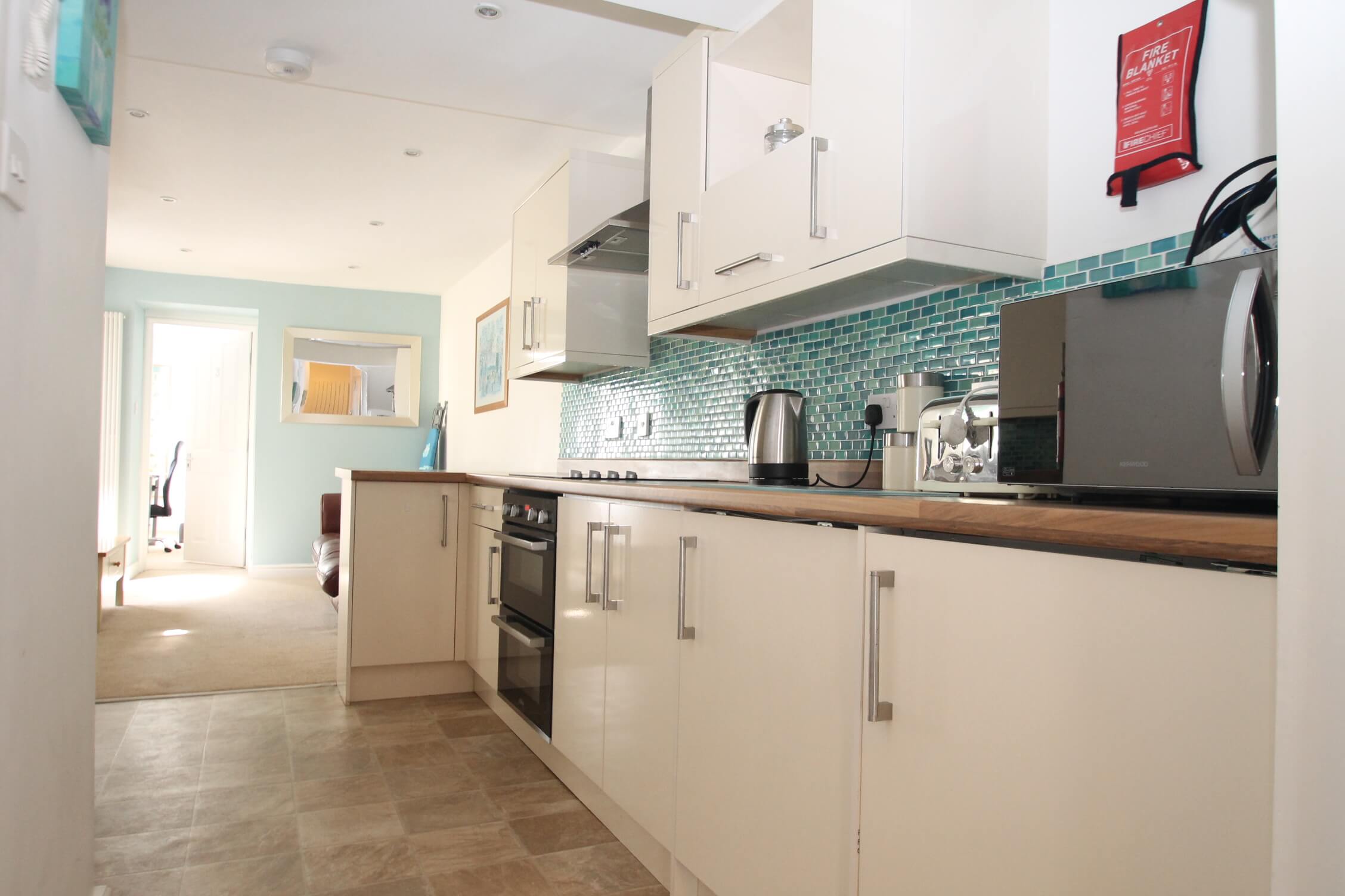 open kitchen and living area with hob and cooker, microwave, leading into living area with brown leather two-seater sofa