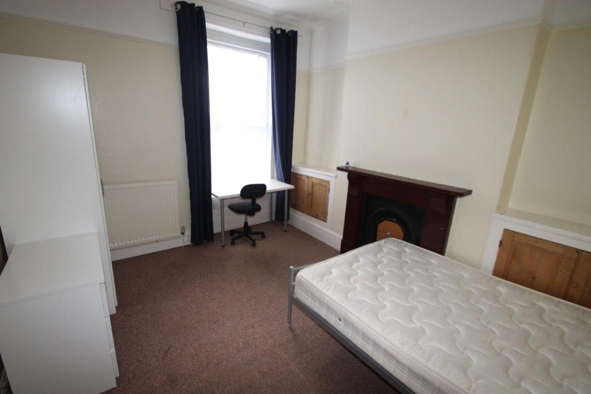 student bedroom with double bed, chest of drawers and desk with office chair in front of window 
