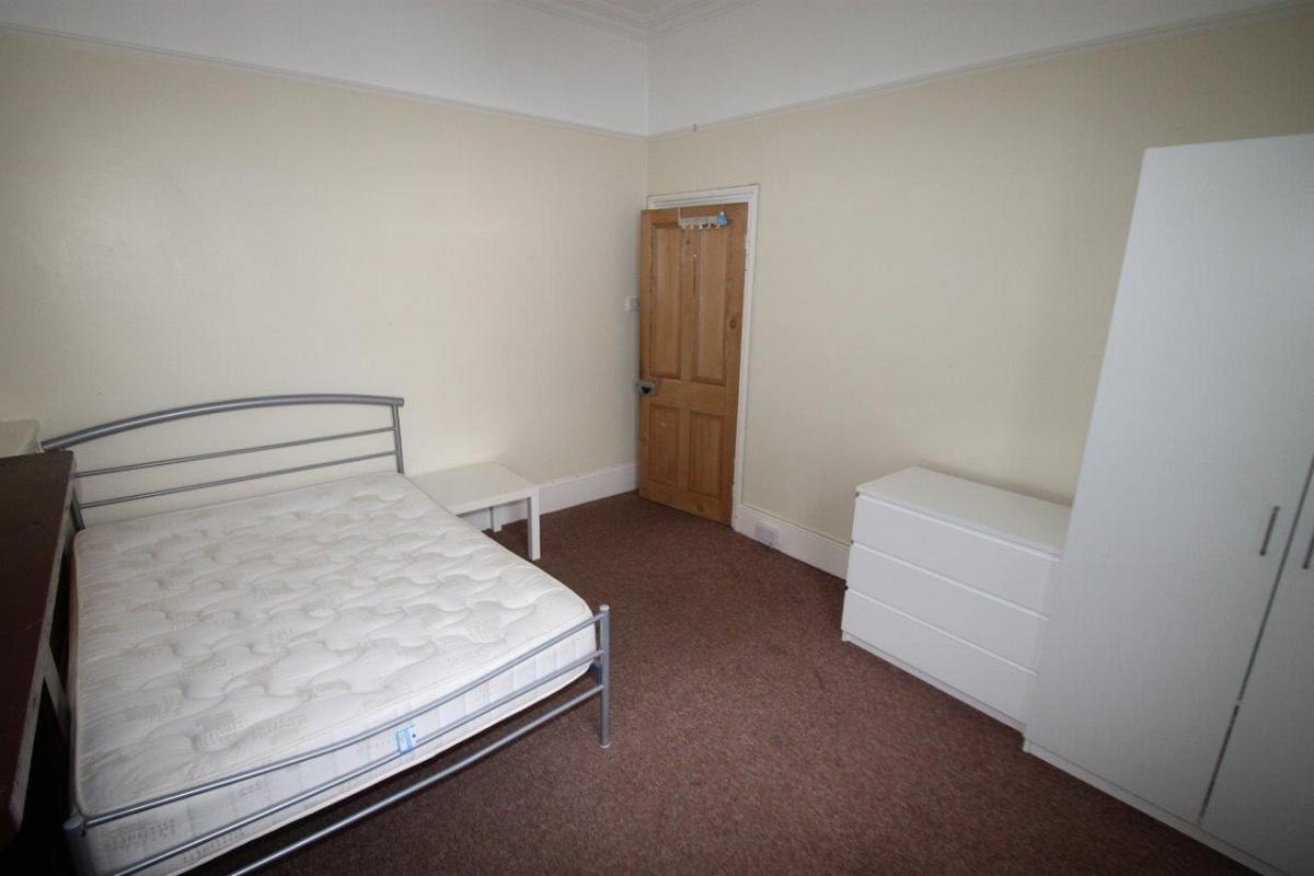student bedroom with double bed, white chest of drawers, two door wardrobe and bedside table