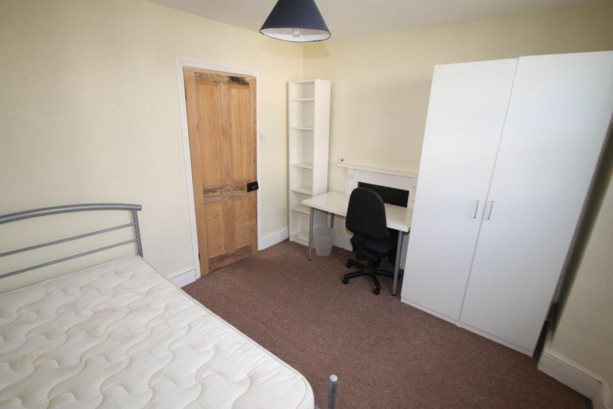 student bedroom with double bed, two door wardrobe, desk with black office chair and tall shelving unit
