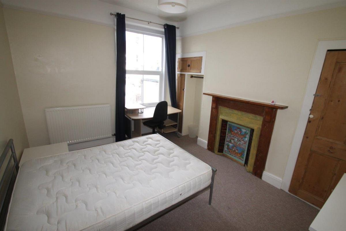 student bedroom with double bed, bedside table, chest of drawers, desk with office chair and clothing rail and storage cupboard