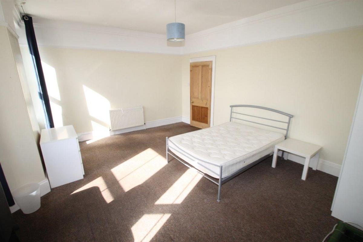 student bedroom with double bed, bedside table, white chest of drawers and two large windows