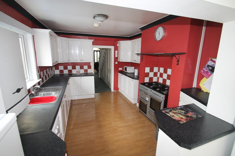 Red walled kitchen with large cooker with gas hobs, washing machine, plenty of work top space and sink, hallway leading to the front of the property