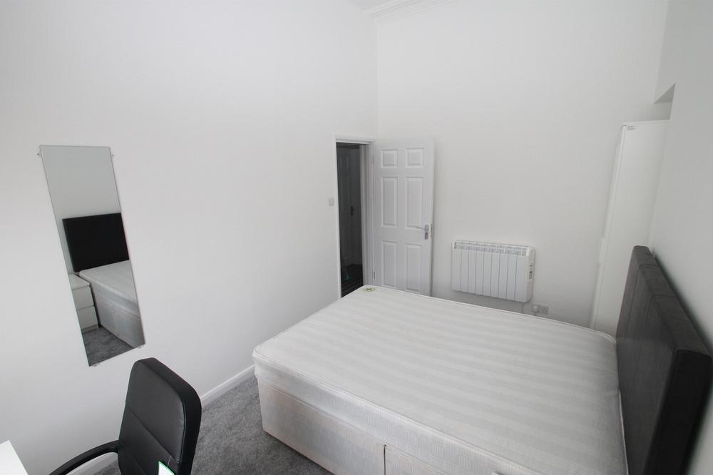 student bedroom with double bed, two door white wardrobe, desk with black office chair and full length mirror