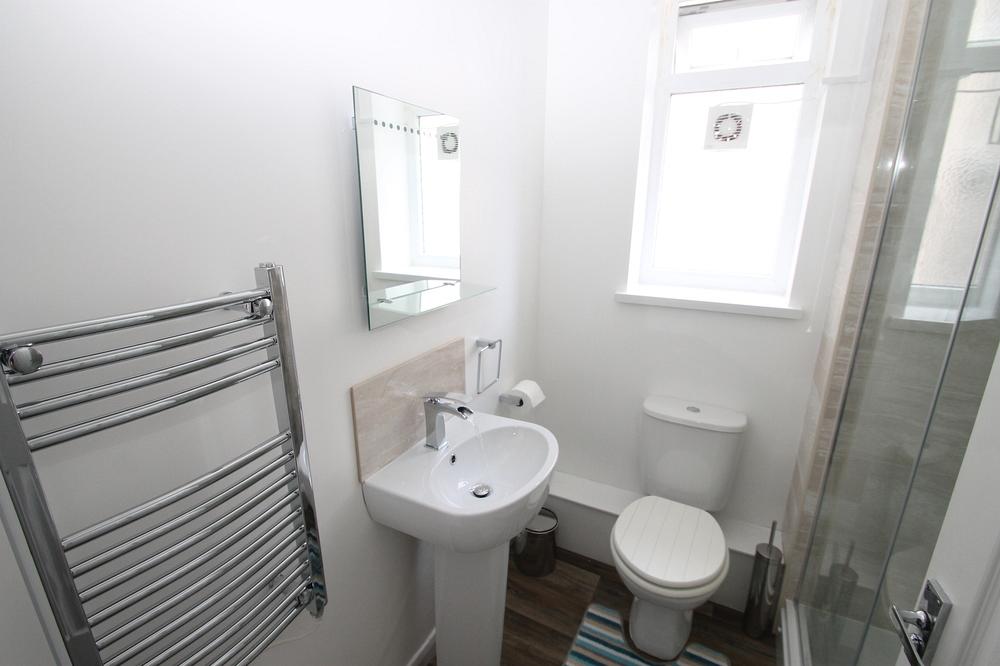 student bathroom with corner shower, mirror and shelf above sink and towel rail radiator