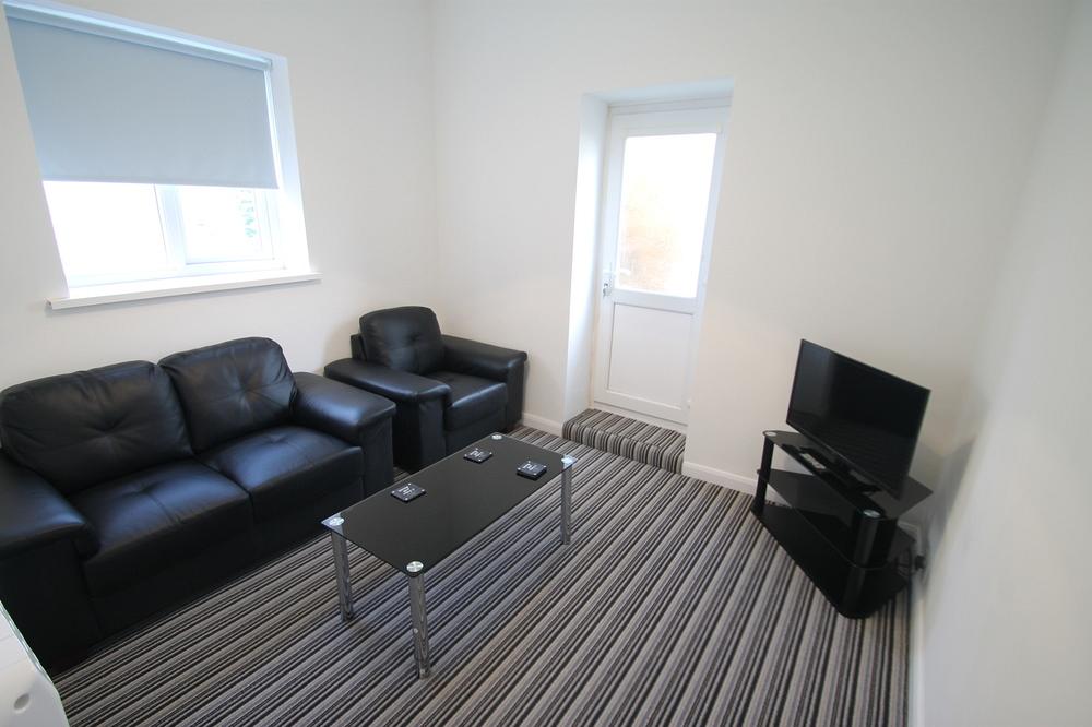 living room with leather 2-seater sofa, black leather armchair, glass coffee table and tv on tv stand
