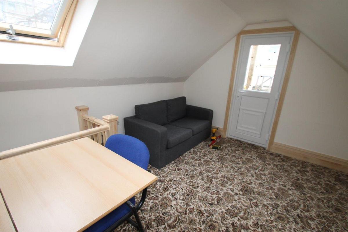 living space with black two-seater sofa, dining table with blue chair and skylgiht window