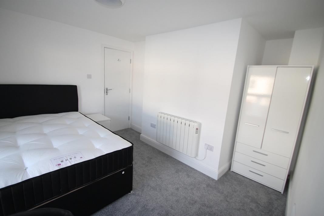 student bedroom with double bed, white bedside table and two door white wardrobe with drawers