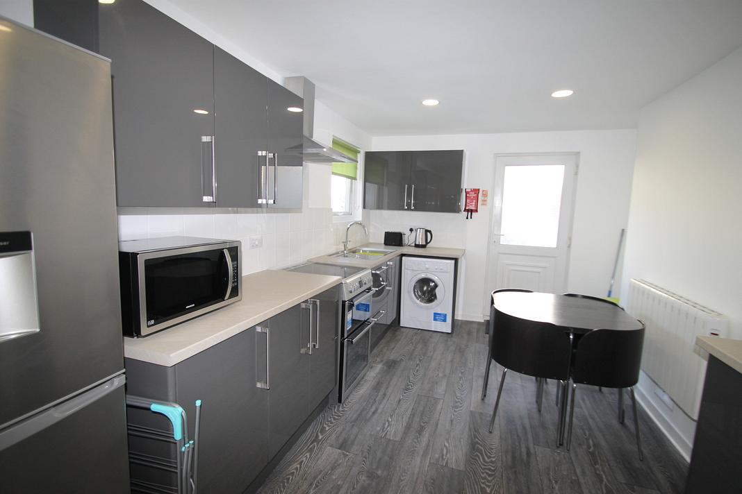 Shared kitchen with fridge freezer, washer/dryer, induction hobs and cooker, microwave and black dining table with four black dining chairs