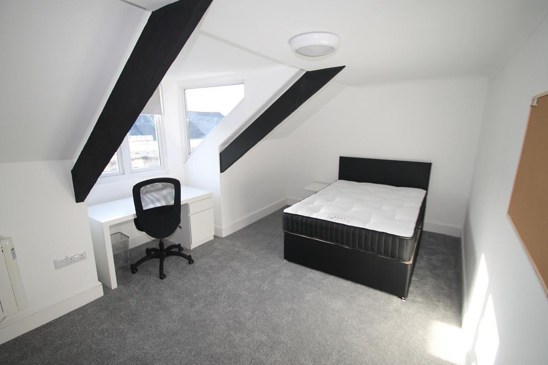 student bedroom with double bed, white desk with black office chair and pinboard on wall