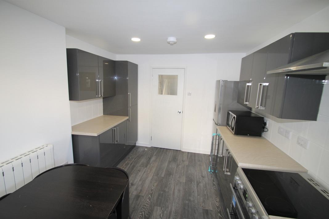 shared kitchen with induction hobs and cooker, black dining table with four black dining chairs, fridge freezer and microwave