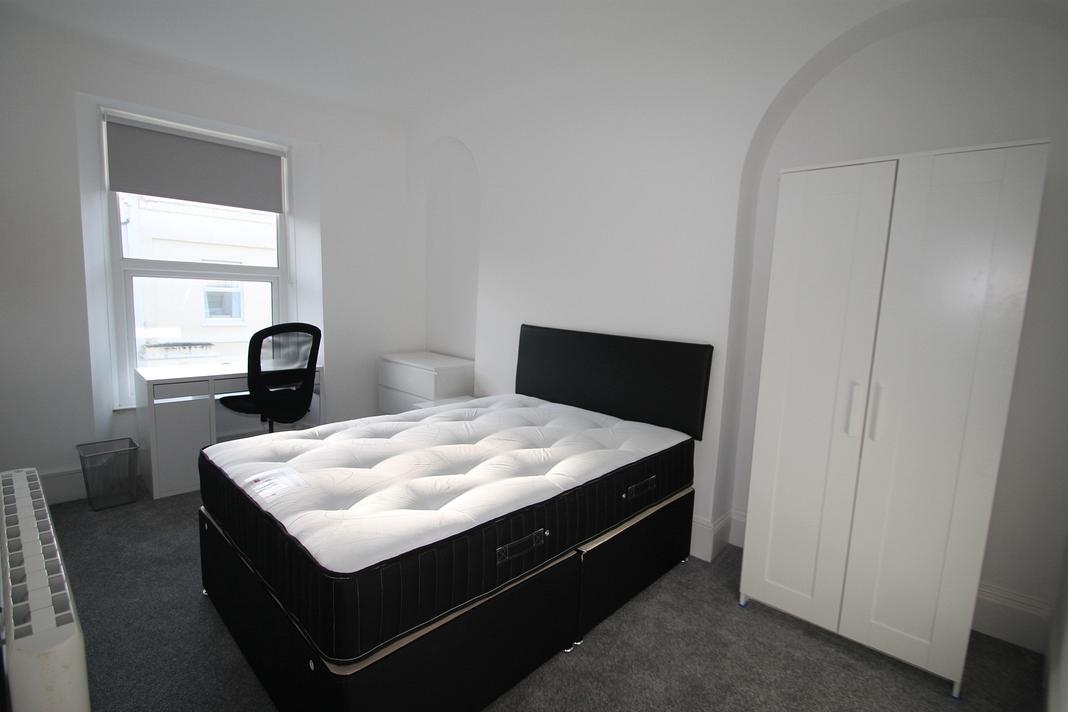 student bedroom with double bed, two door wardrobe, chest of drawers and white desk with black office chair