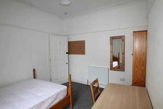 student bedroom with double bed, full length mirror, two door wardrobe, desk with chair and pinboard on wall