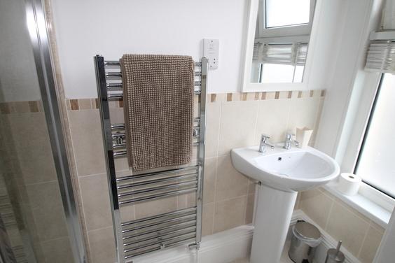 shared bathroom with corner shower, mirror above sink and towel rack radiator