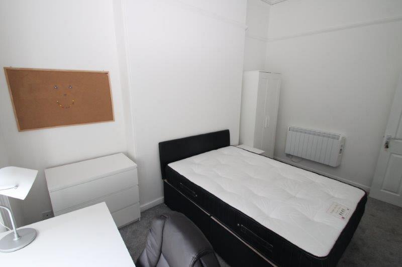 student bedroom with double bed, chest of drawers, two door wardrobe, bedside table, desk with black office chair and pinboard on wall