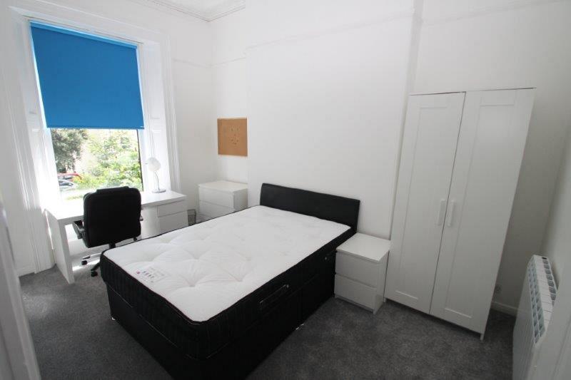 student bedroom with double bed, white two door wardrobe, chest of drawers, bedside table and desk with black office chair