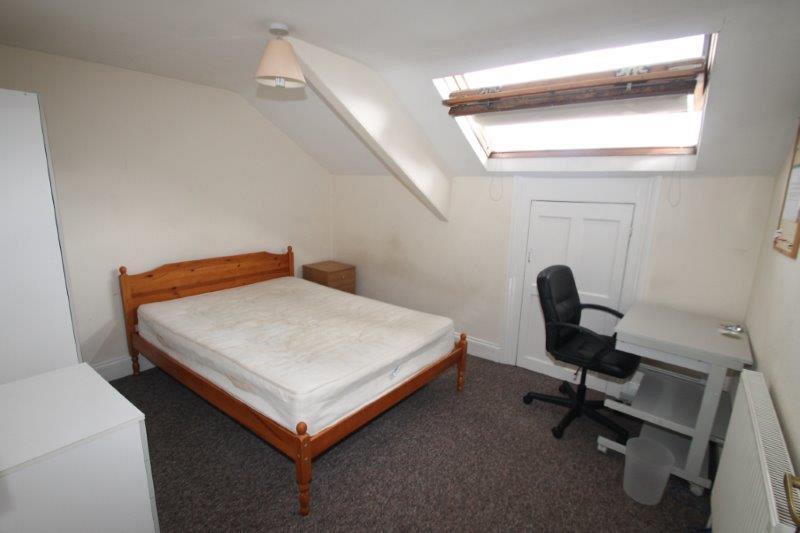 student bedroom with double bed, two door wardrobe, chest of drawers, bedside table, desk with black office chair and large skylight