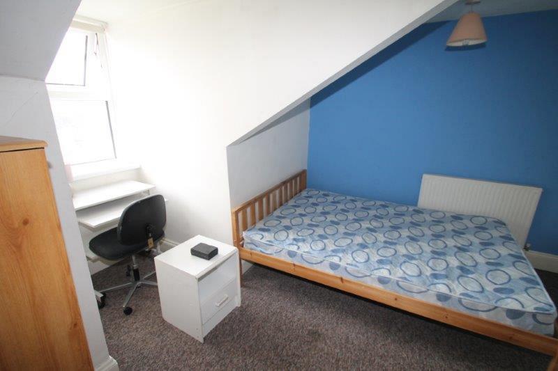student bedroom with double bed, chest of drawers, two door wardrobe with drawers, bedside table and desk with office chair in front of large window
