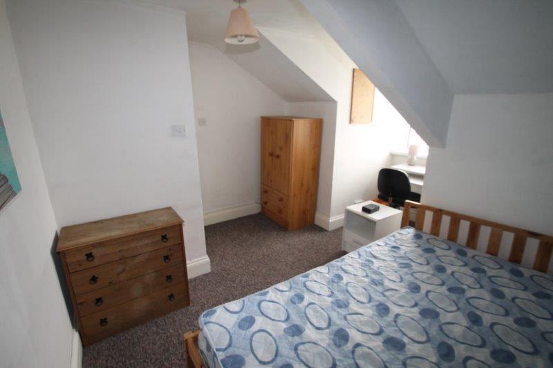 student bedroom with double bed, chest of drawers, two door wardrobe with drawers, bedside table and desk with office chair in front of large window