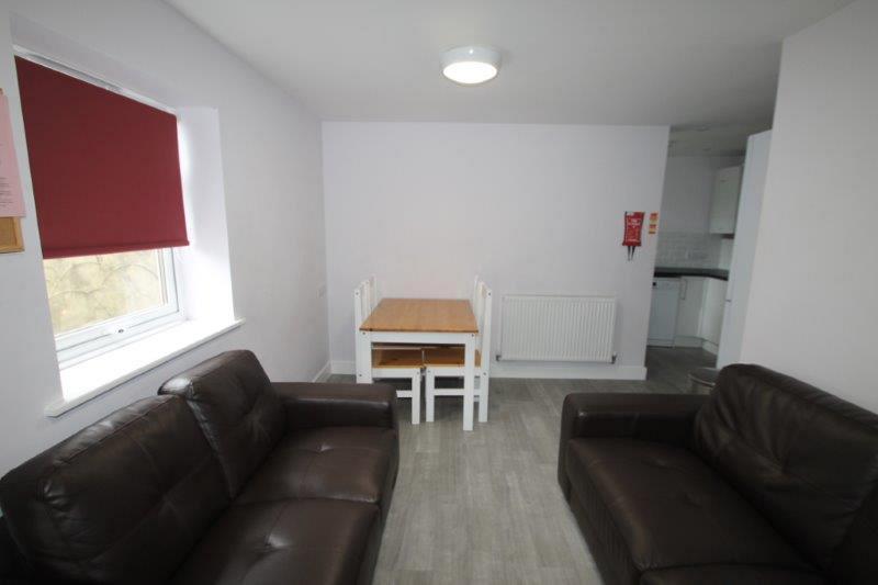 Living area with two black two-seater sofas, dining table with four dining chairs leading into kitchen